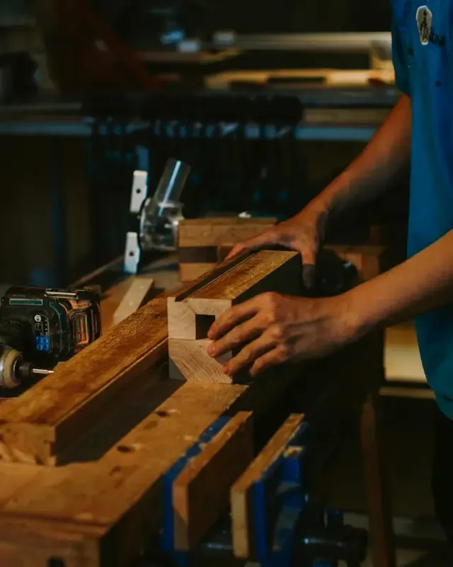 Artisan menuisier ajustant une pièce de bois sur un établi équipé d’outils électroportatifs