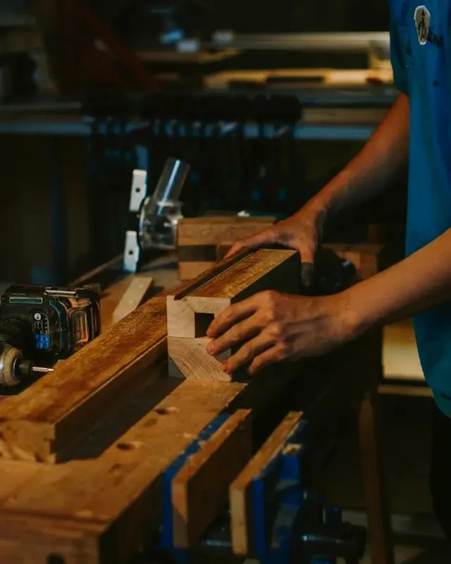 Artisan menuisier ajustant une pièce de bois sur un établi équipé d’outils électroportatifs