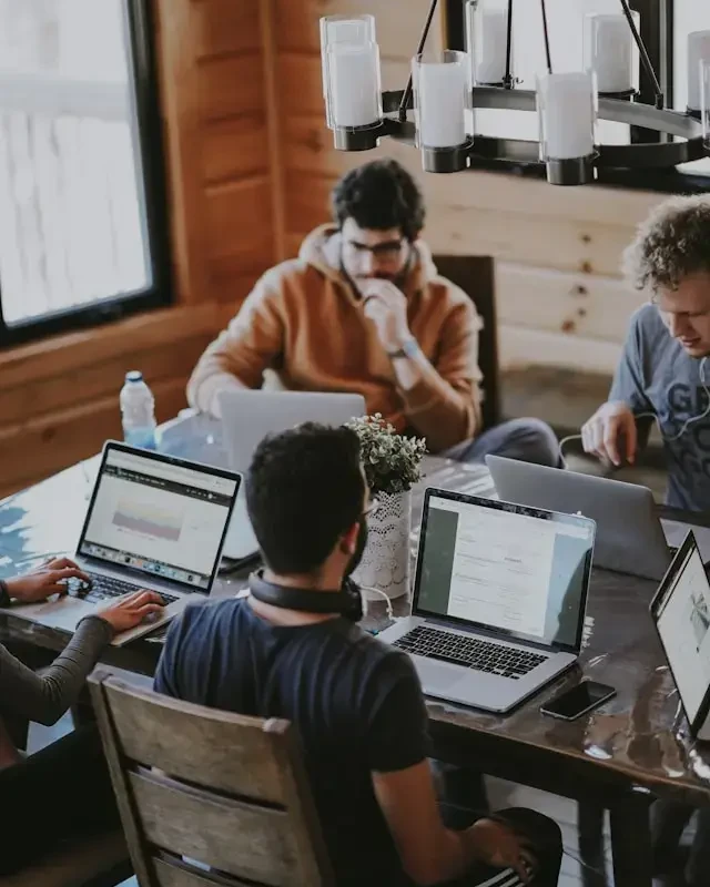 Quatre personnes travaillant ensemble sur leurs ordinateurs portables autour d’une table