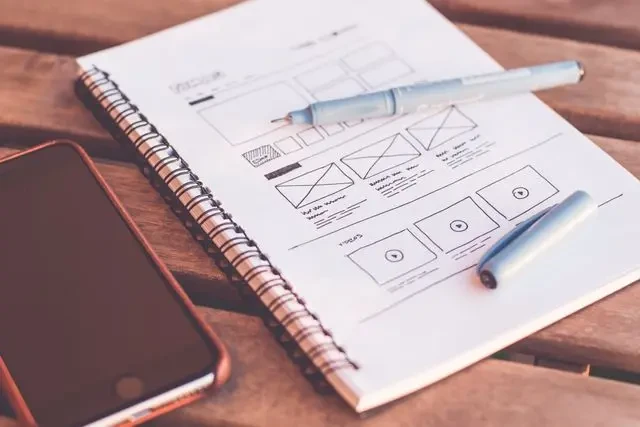 Croquis d’une maquette de site web dessinée à la main dans un carnet, à côté d’un smartphone