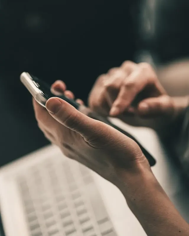 Mains tenant un smartphone à côté d’un clavier d’ordinateur portable