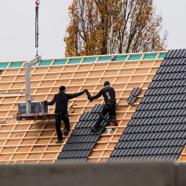 Deux couvreurs posant des tuiles noires sur une toiture en chantier