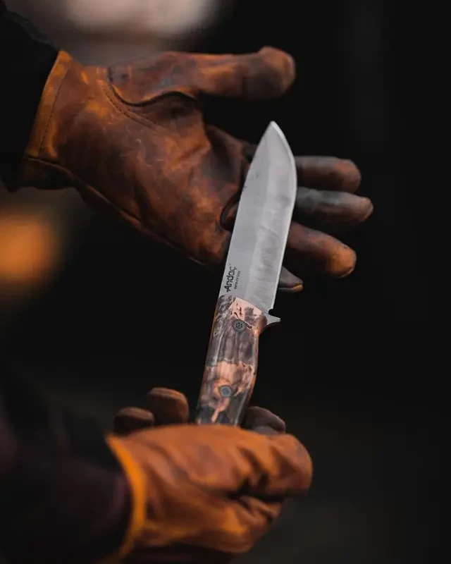 Mains gantées de cuir tenant un couteau artisanal fraîchement forgé
