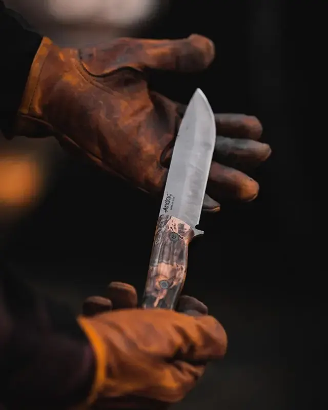 Mains gantées de cuir tenant un couteau artisanal fraîchement forgé